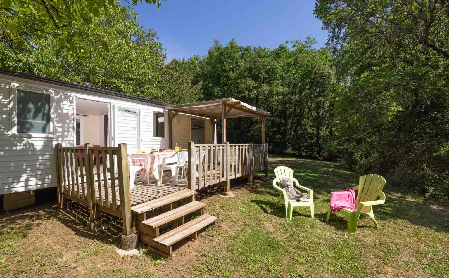Mobil-home avec terrasse en bois couverte et salon de jardin sous les chênes au camping le Picouty