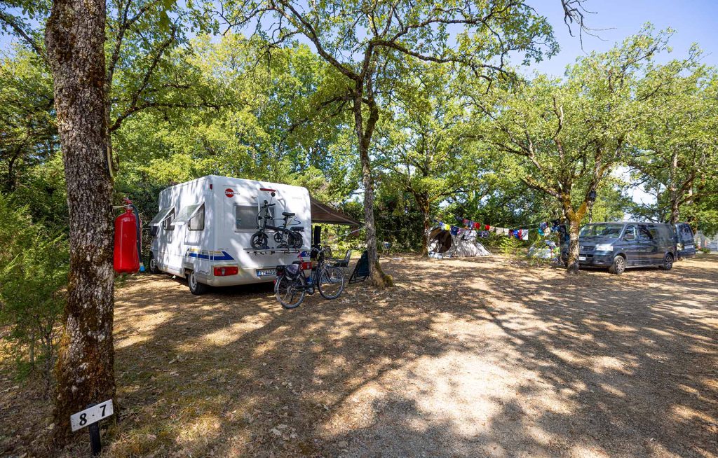 Camping-car et tente installés sur des emplacements ombragés sous les chênes au camping le Picouty dans le Lot
